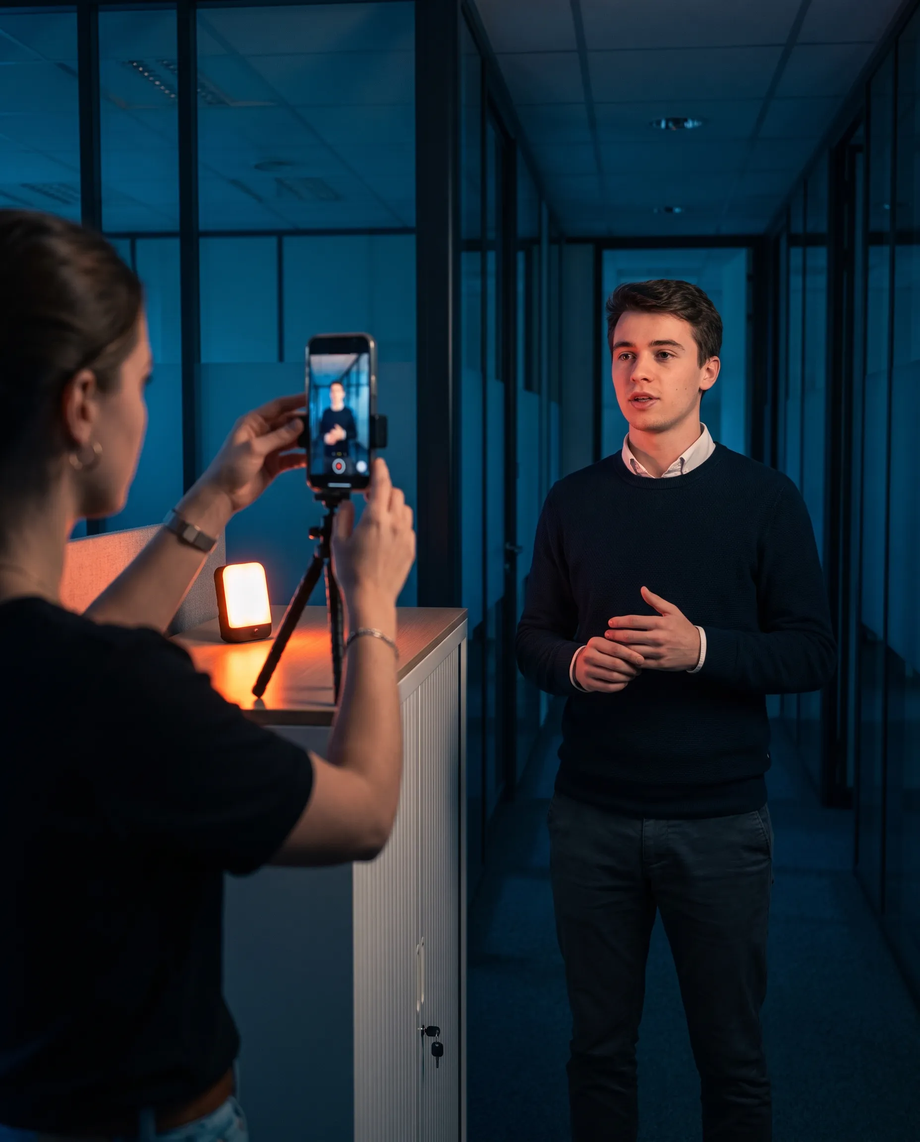 Tournage d’un format vertical au smartphone sur mini-trépied : un collaborateur s’exprime dans un couloir de bureaux vitré